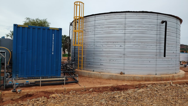 Kurmuk case-study photograph: steel water tank and blue treatment container